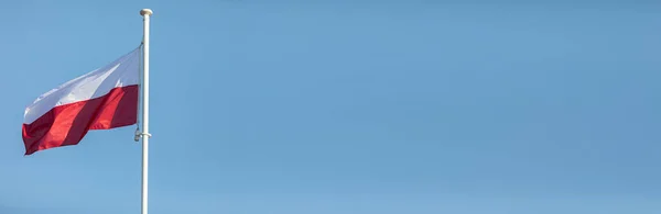 Польский флаг, развевающийся на ветру на высокой мачте на фоне голубого неба. Панорама. — стоковое фото