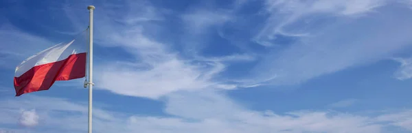 На фоне голубого неба и нескольких белых облаков развевается национальный флаг Польши. Панорама. — стоковое фото