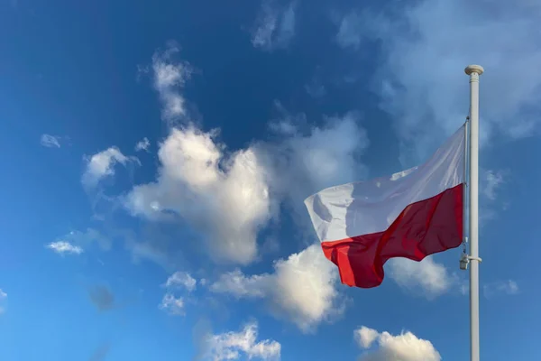 Η εθνική σημαία της Πολωνίας κυματίζει ενάντια σε ένα γαλάζιο ουρανό και μερικά άσπρα σύννεφα. — Φωτογραφία Αρχείου