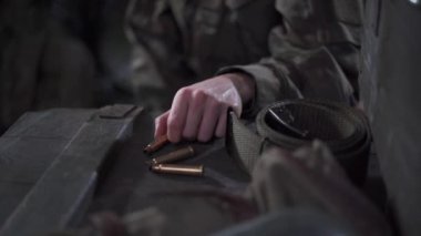 Bir kadın mühimmat kutusunun yanında otururken tüfek kovanlarıyla oynuyor..