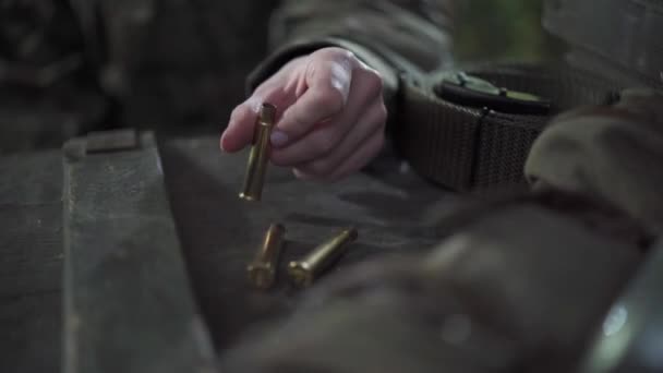 Uma mulher brinca com cartuchos de espingarda enquanto está sentada junto a uma caixa de munição. — Vídeo de Stock