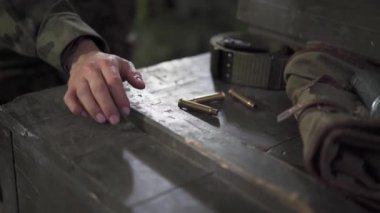 Bayan asker elini sandığa koyar ve mermileri toplar ve sonra gergin bir şekilde fırlatır..