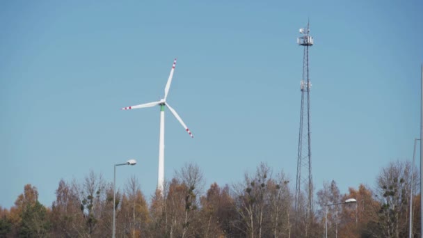 Una turbina eolica su una collina tra gli alberi. Una torre di trasmissione del cellulare. — Video Stock