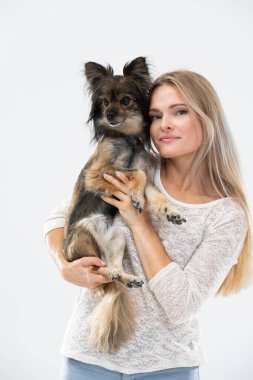 A blonde woman with long hair holds a small dog in her arms and looks at it. Multi-breed dog.