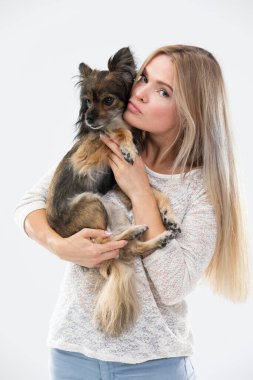 A blonde woman with long hair holds a small dog in her arms and looks at it. Multi-breed dog.