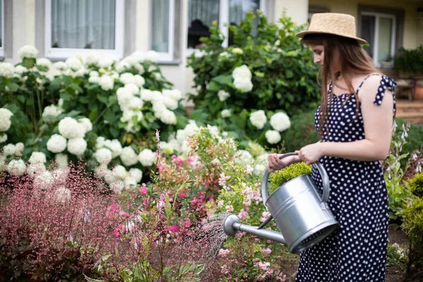 A young girl waters the flowers in her garden with a watering can. — Stock Photo, Image