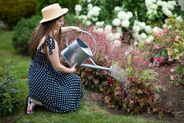A young girl kneels down and waters the flowers in her garden with a watering can. — Stock Photo, Image