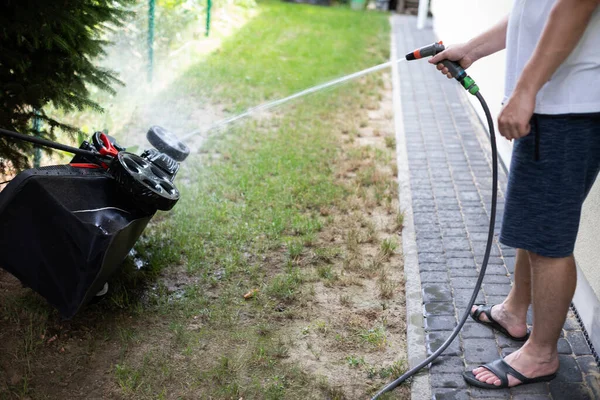 A man washes a lawn mower with a stream of water. — Stock Photo, Image