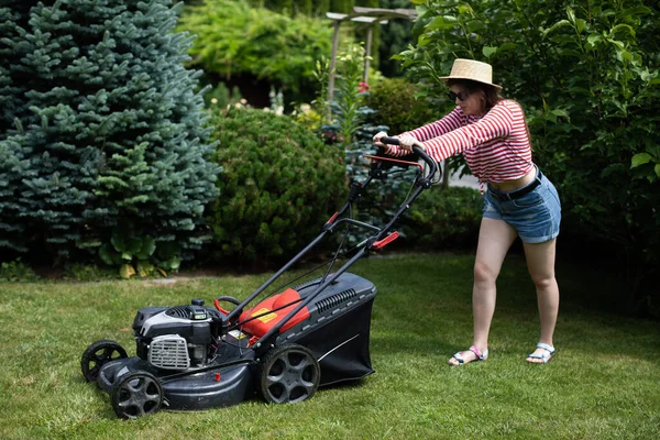 Een jonge vrouw maait gras met een tuinmaaier op een hete zomerdag. — Stockfoto