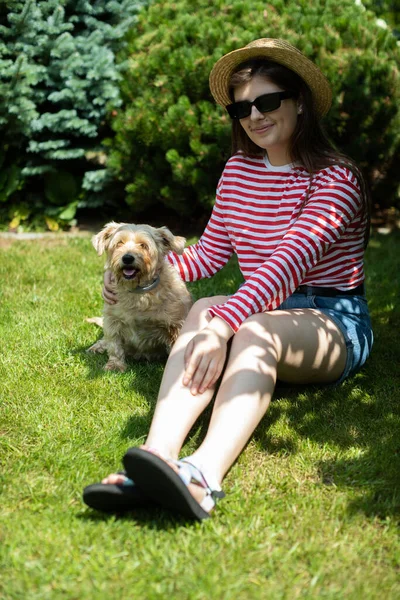 Una chica se sienta en la hierba a la sombra con su perro. — Foto de Stock