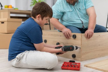 Bir oğul katlanan bir kitaplıkta tornavidayla vidayı sıkıyor..