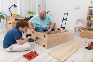 Oğlu tornavidayla vidaları vidalıyor, babası da kitaplığı tutuyor..