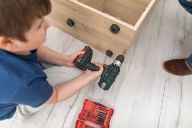 Genç bir çocuk kablosuz tornavidayla vidaları sıkıyor..