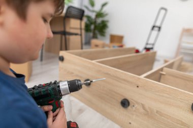 Genç bir çocuk elinde kablosuz bir tornavida tutuyor ve merak ediyor..