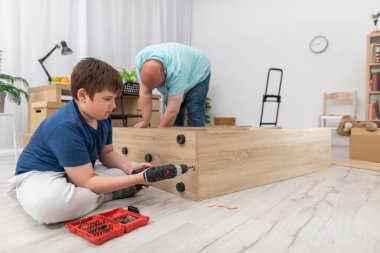 Oğlu tornavidayla vidaları vidalıyor, babası da kitaplığı tutuyor..