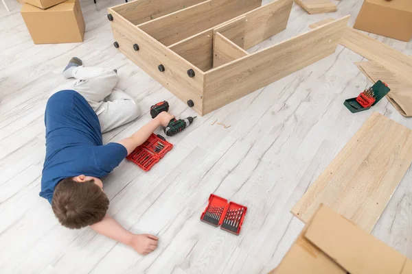 Un joven se duerme en el suelo mientras monta muebles. — Foto de Stock