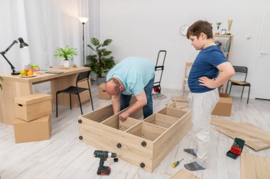 Babam mobilyaları monte ediyor ve oğlu da montaj sürecini denetliyor..