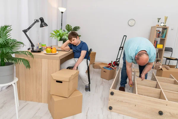 Papai monta uma estante e filho estuda em sua mesa. — Fotografia de Stock