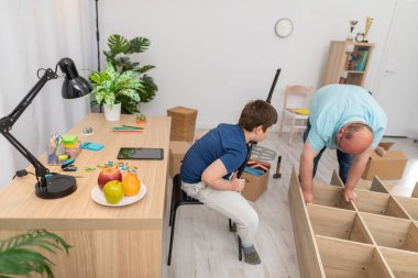 Baba gayretli bir şekilde mobilya monte ediyor ve oğlu sadece izliyor. Mobilya montajı.