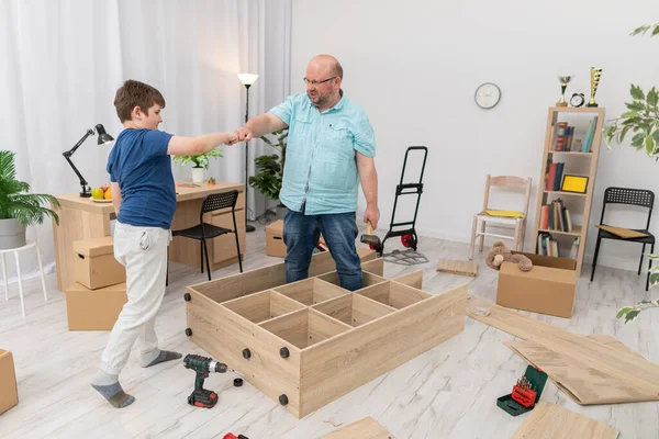 Pai e filho fazem um gesto de tartaruga enquanto montam móveis. — Fotografia de Stock