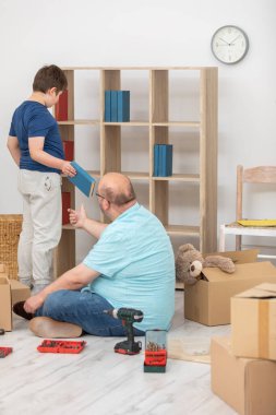 Baba ve oğul taşındıktan hemen sonra kitaplığa kitap koyarlar..