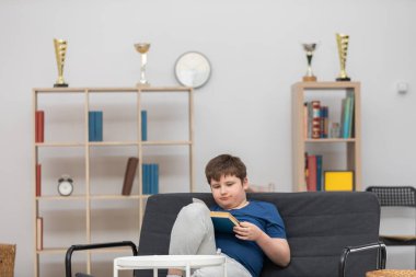 Genç bir çocuk kanepede oturmuş kitap okuyor..