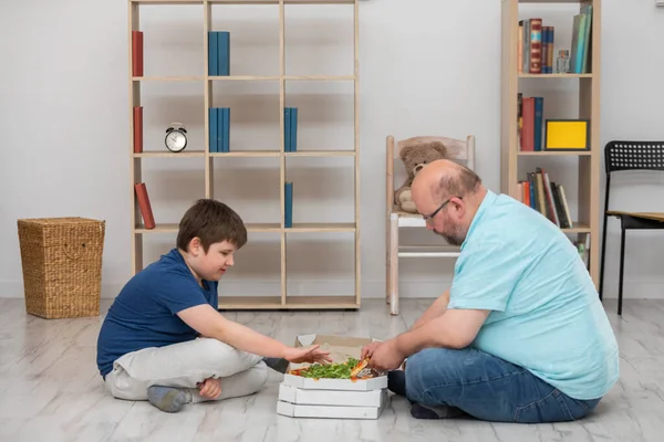 Sentados no chão, pai e filho escolhem fatias de pizza. — Fotografia de Stock