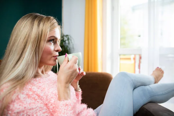 Молода жінка п'є каву, сидячи у вітальні . — стокове фото