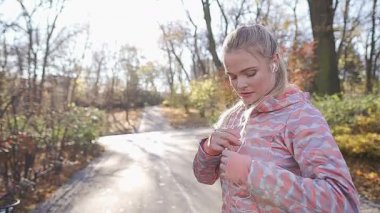 Bir kız parkta sabah koşusundan önce müziği ayarlar..