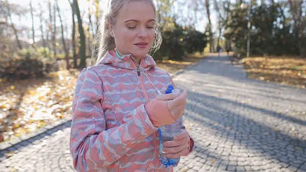 Een jonge vrouw opent een plastic fles na een run en drinkt water. — Stockvideo