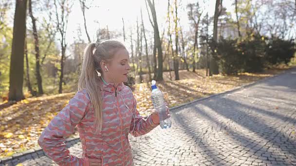 Una chica se toma un descanso de su carrera matutina para beber agua. — Vídeo de stock