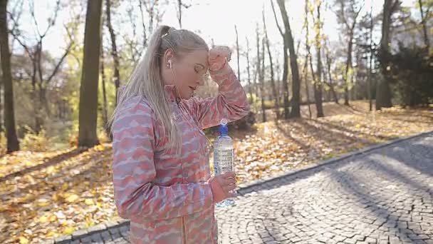 Una chica monstruosamente cansada bebe agua. Correr por la mañana. — Vídeo de stock