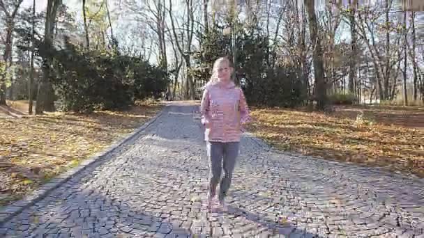 Una ragazza corre nel parco e agita la mano ad un amico. — Video Stock