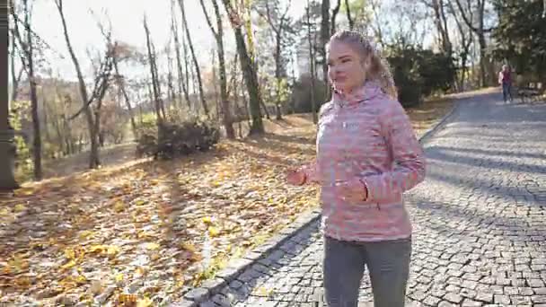 Une femme blonde souriante court dans un parc de la ville, en automne. — Video