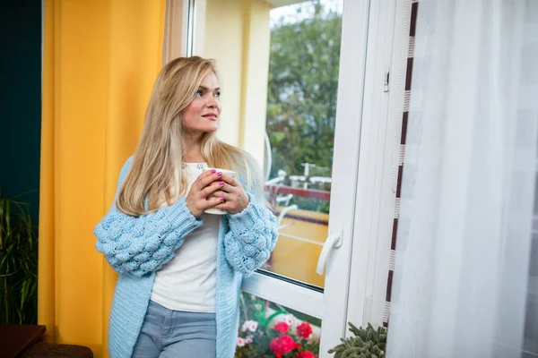 A menina fica na janela com seu café e olha para fora. — Fotografia de Stock