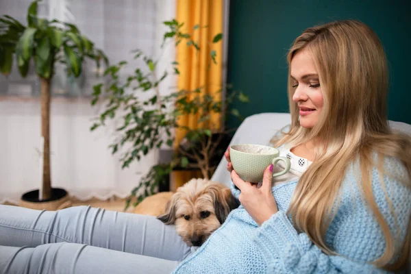 Дівчина сидить на дивані з чашкою кави і собака лежить поруч з нею . — стокове фото