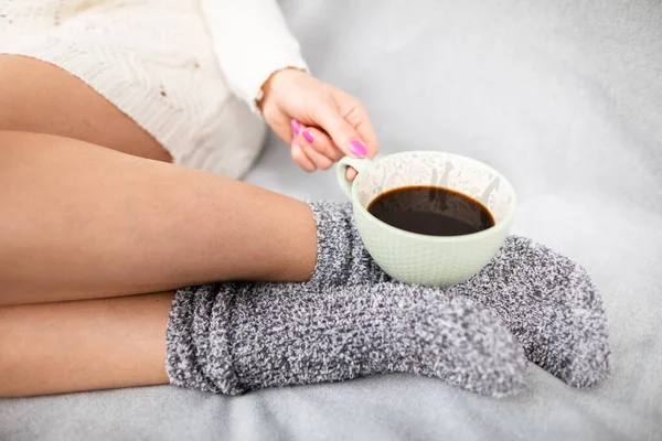 Pernas finas em meias de lã. Uma xícara de café nas mãos de uma mulher. — Fotografia de Stock