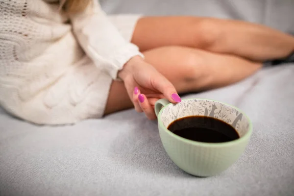 Mulher senta-se na cama com uma xícara de café. Pernas limpas. — Fotografia de Stock