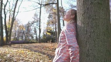 Ağaca yaslanmış gülümseyen bir sarışın etrafına bakıyor..