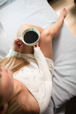 İnce bacaklar. Yukarıdan çerçevelenmiş bir kadın elinde bir fincan kahve tutarken.