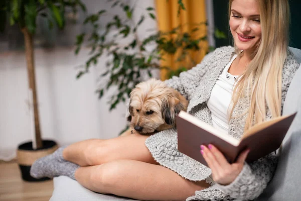 Дівчина читає книжку з посмішкою на губах. Багаторасовий собака . — стокове фото
