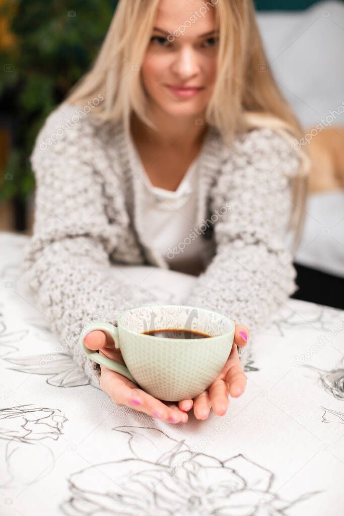 An attractive young woman holds a cup of coffee in her retracted hands.