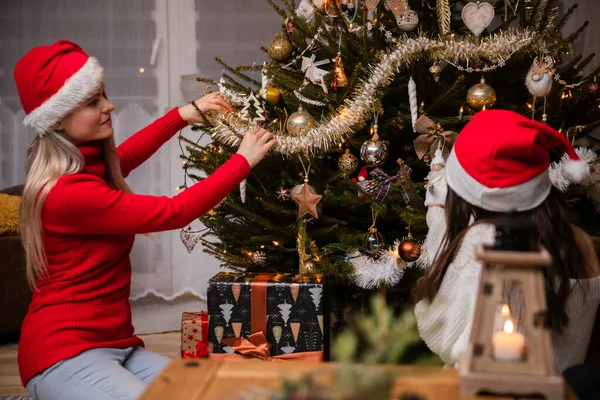 Las niñas que usan sombreros rojos de Santa adornan un árbol de Navidad. — Foto de Stock