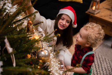 Genç bir kız kardeş erkek kardeşine Noel ağacındaki süsleri gösterir..