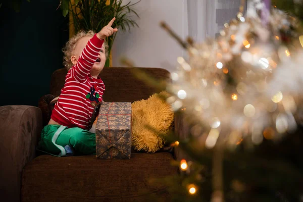 A smiling two-year-old child points his finger at a Christmas tree. — Stock Photo, Image