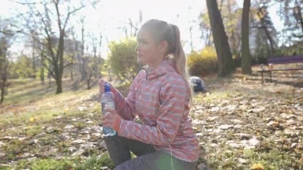 Девушка ставит пластиковую бутылку с водой на лужайку городского парка. — стоковое видео