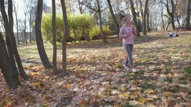 Una chica camina por el parque y corrige los auriculares en sus oídos. — Vídeo de stock