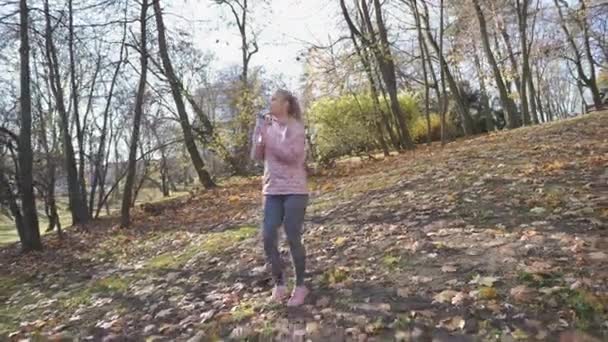 Een tevreden meisje loopt in het park en nipt water uit een fles. — Stockvideo