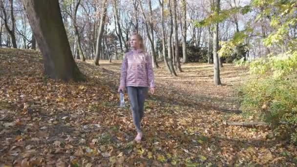 Una ragazza soddisfatta cammina nel parco e sorseggia acqua da una bottiglia. — Video Stock