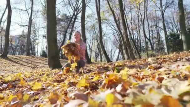 Dívka v městském parku vyhazuje podzimní listí do vzduchu. — Stock video
